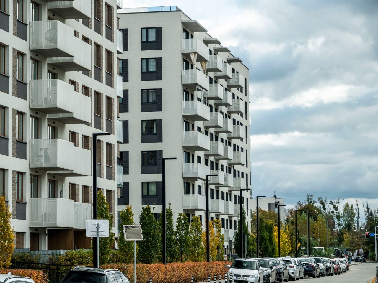 services-02 Contemporary apartment complex on a city street lined with parked cars and autumn foliage.